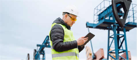 An oilfield worker in high viz PPE checks local emissions on a tablet.